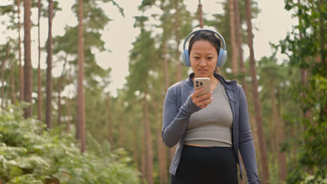 Mujer-Con-Auriculares-Inalámbricos-Haciendo-Ejercicio-Al-Aire-Libre,-Transmitiendo-Música-O-Podcast-Desde-Un-Teléfono-Móvil,-Corriendo-Por-Una-Pista-En-El-Bosque-Con-Ropa-Deportiva,-Filmada-En-Tiempo-Real-1